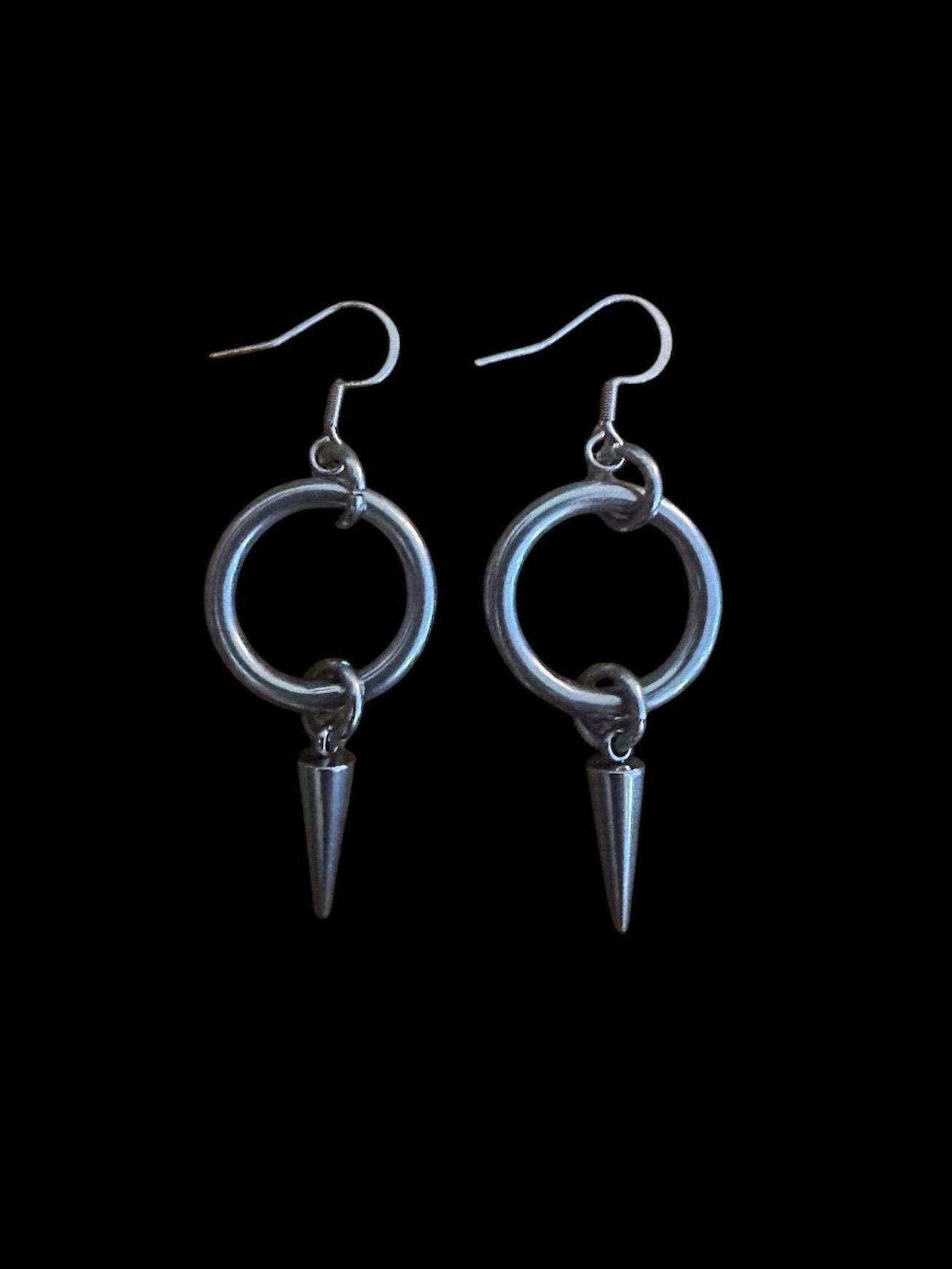 May include: A pair of silver hoop earrings with a pointed spike hanging from each hoop.