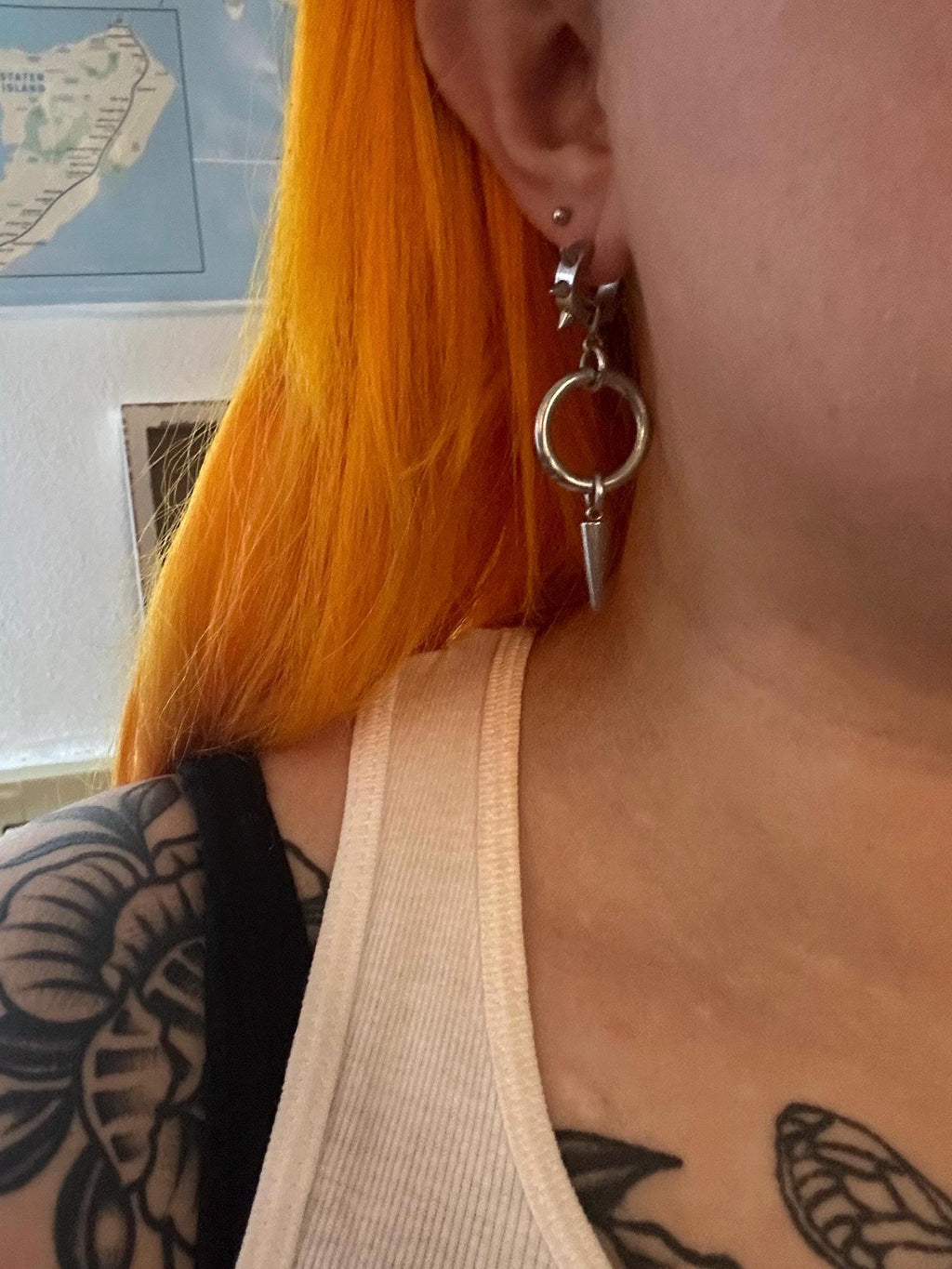 May include: A silver hoop earring with a dangling spike charm and a smaller hoop charm.